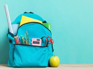 Blue school backpack sitting on floor, with stationary and green apple.